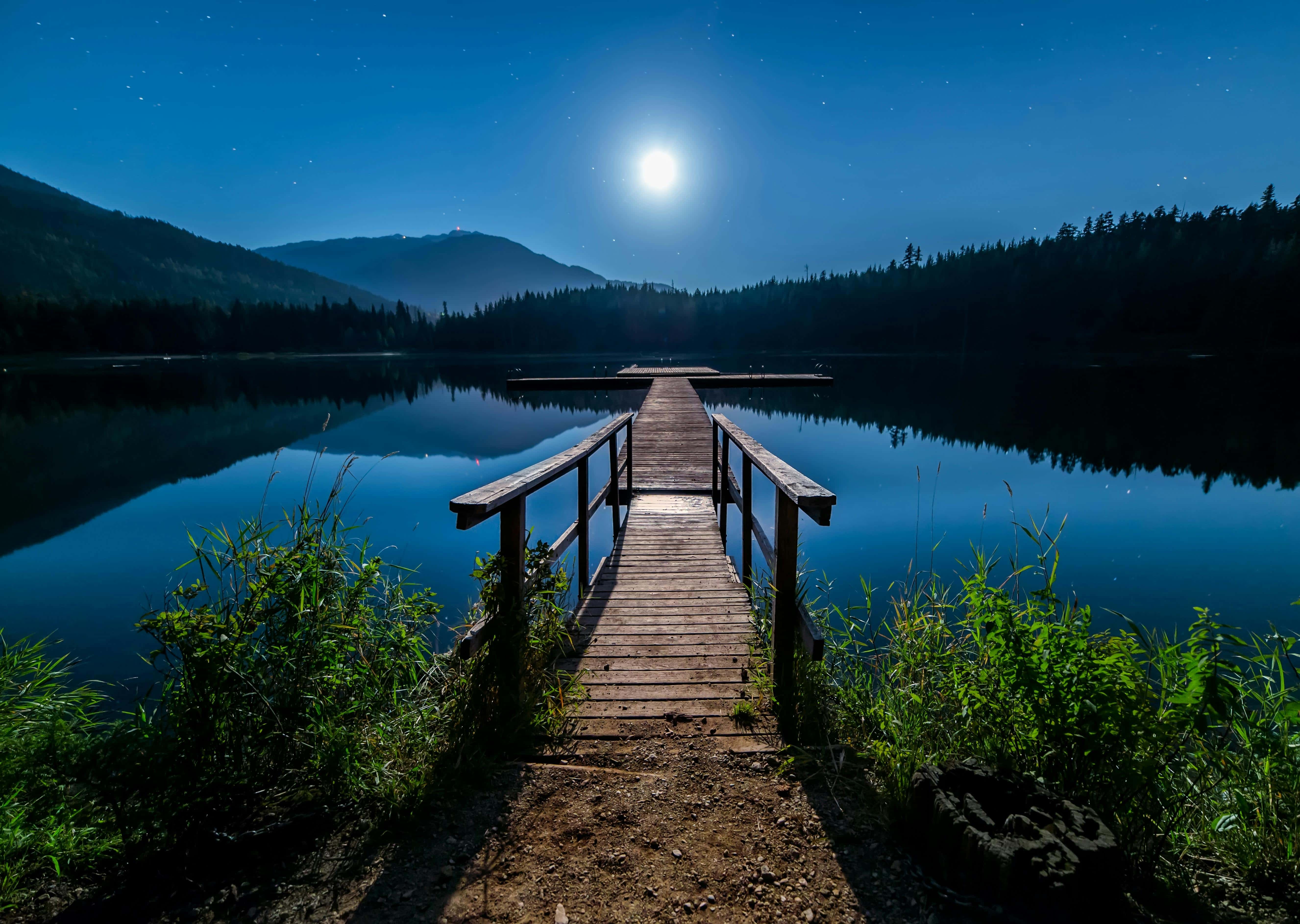 The sun shines brightly over a still lake, casting reflections on the water near a wooden dock.